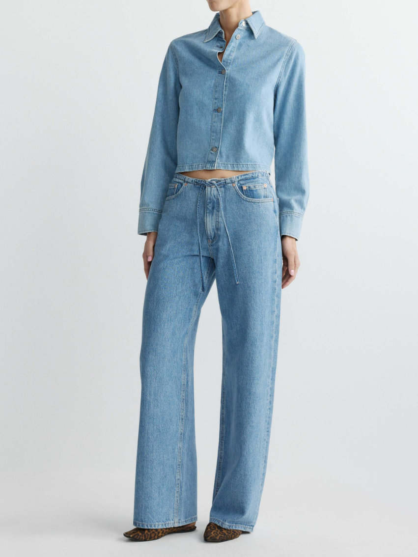 Person wearing a light blue denim jacket and jeans on a white background