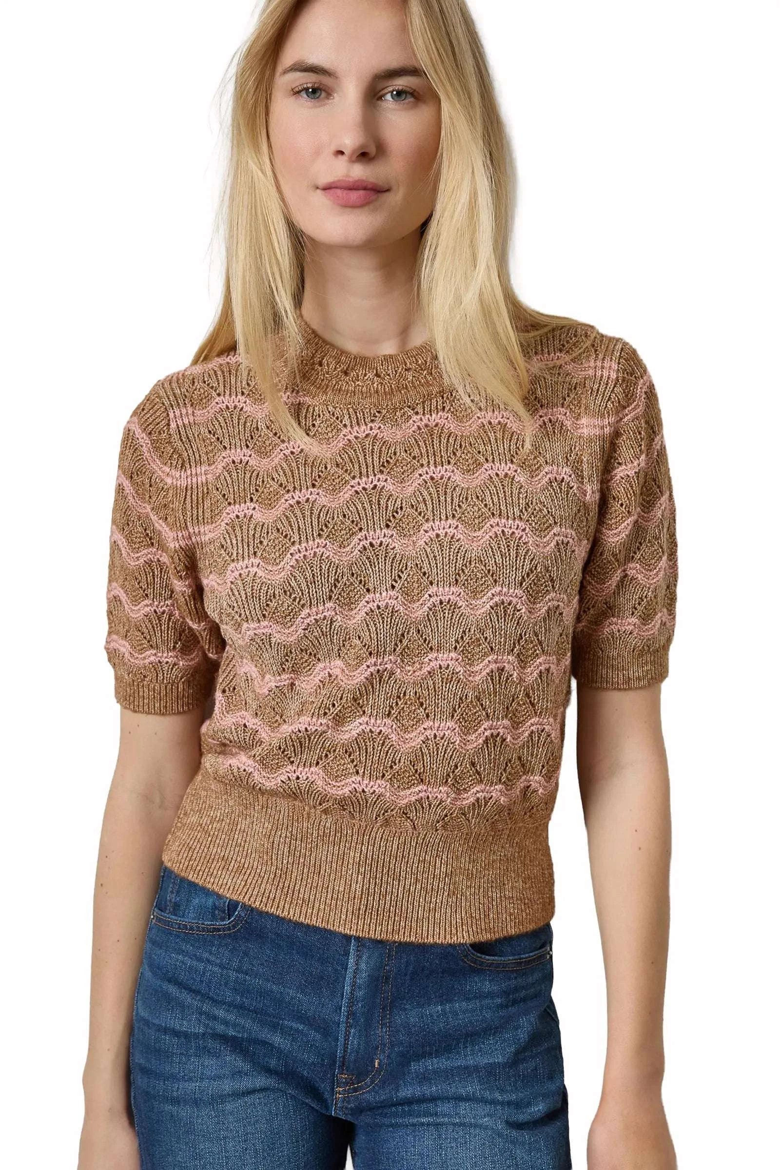 A woman wearing a short-sleeve knit sweater with a wavy, scallop-like pattern in brown and dusty pink, paired with blue jeans, against a plain white background.