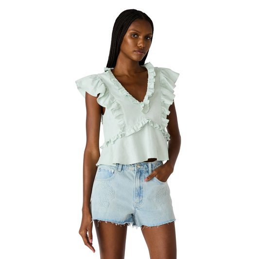 Woman wearing a light green ruffled top and denim shorts on a white background