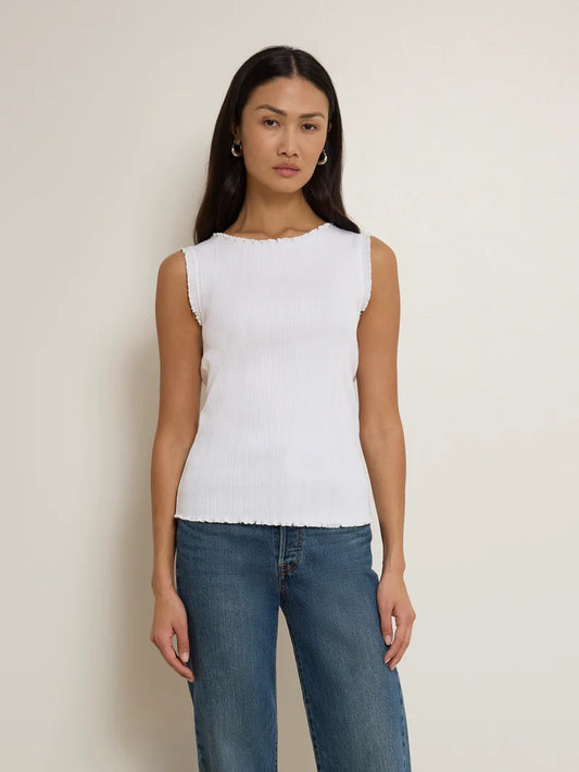 Woman wearing a white sleeveless top and blue jeans against a plain background