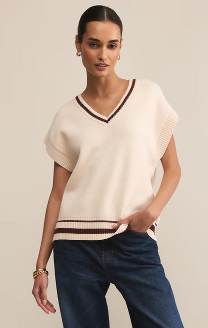 Woman wearing a cream-colored sweater with brown trim against a beige background