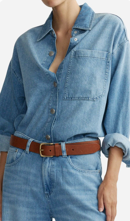 Person wearing a blue denim shirt and jeans with a brown belt on a white background