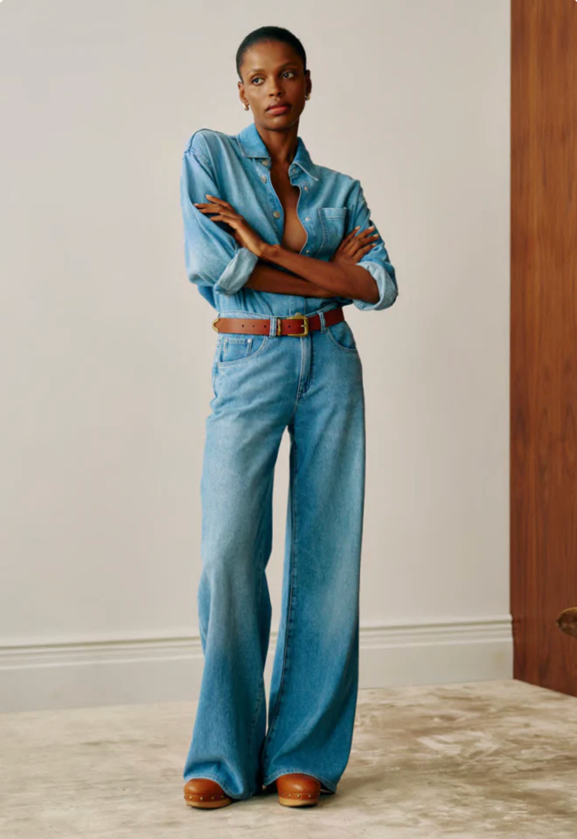 Person wearing a blue denim outfit with a belt, standing against a neutral wall.
