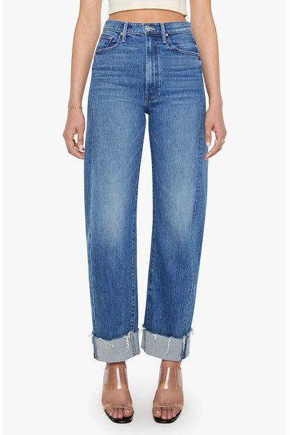 A model wearing a pair of high-waisted, wide-leg blue jeans with a faded wash and rolled cuffs, paired with clear high-heeled sandals against a plain white background.