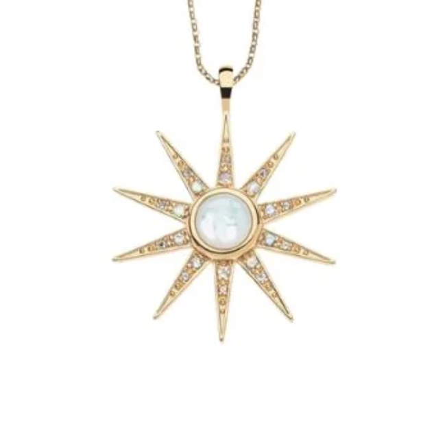 A gold starburst pendant necklace featuring a central round white mother-of-pearl cabochon and small clear pavé stones along the points, suspended from a delicate gold chain against a plain white background.