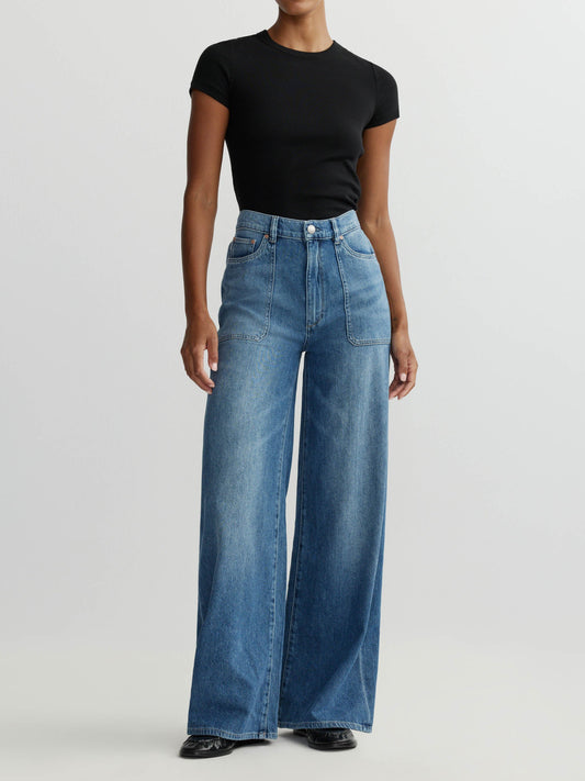 Person wearing blue wide-leg jeans and a black top on a white background
