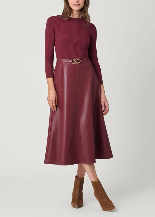 A woman models a burgundy ribbed knit long-sleeve top paired with a matching faux-leather midi skirt featuring a gold-tone belt, styled with brown suede ankle boots against a light gray studio background.