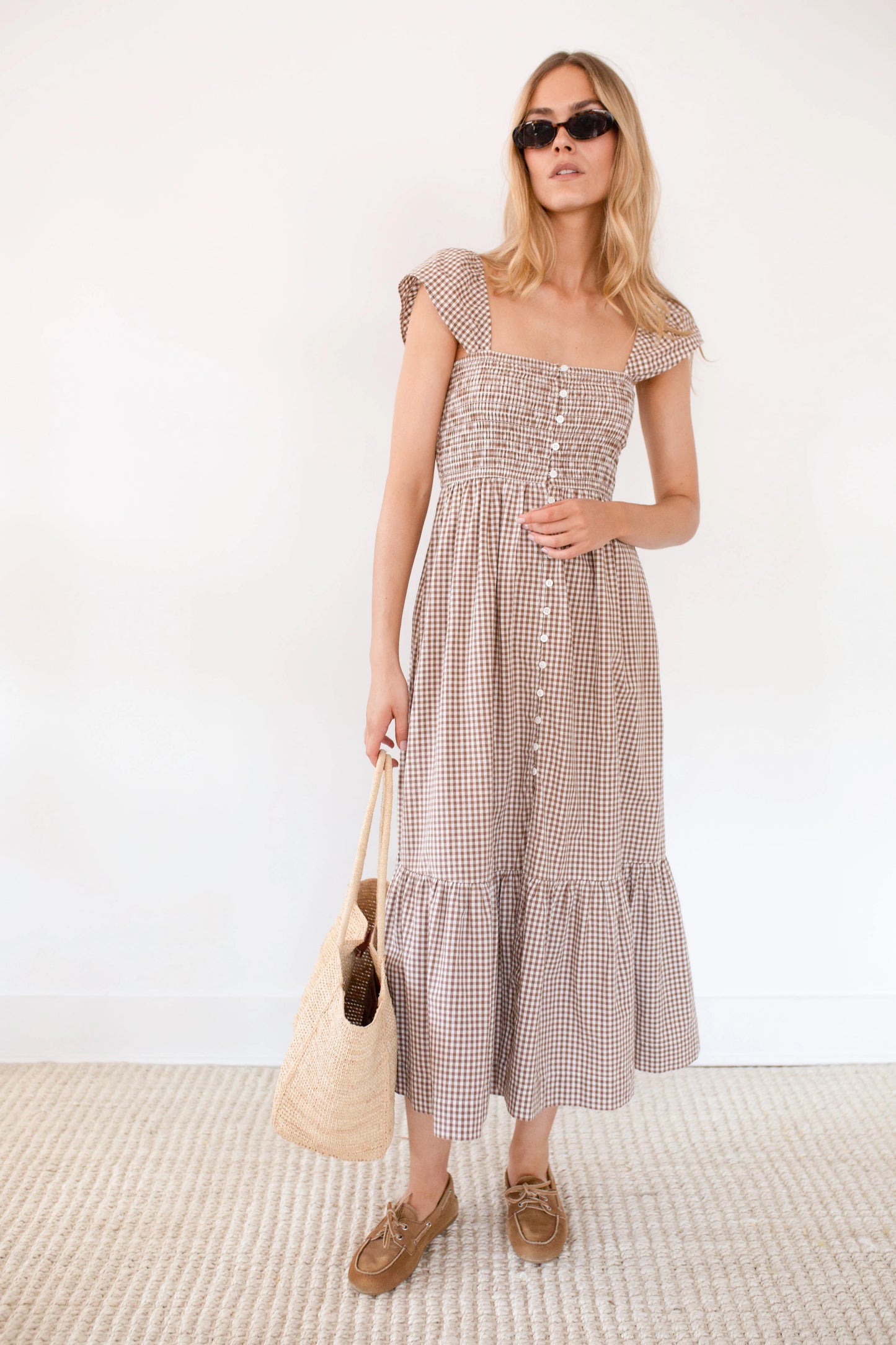 Woman wearing a checkered dress holding a beige bag against a white background