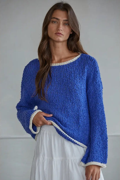 Woman wearing a blue knitted sweater with white trim against a plain background