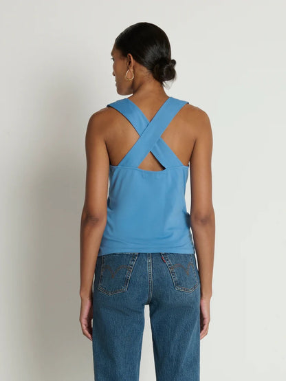 Person wearing a blue tank top with crossed straps and blue jeans on a plain background