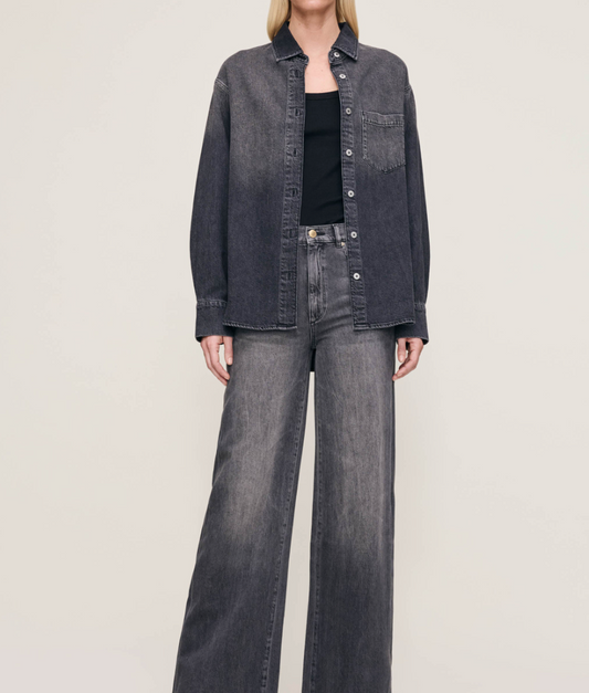Person wearing a dark denim jacket and jeans on a plain background