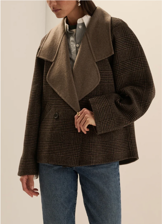 A model wearing a brown and black plaid double-breasted coat with a large brown woolen collar, styled with a striped shirt and blue jeans.