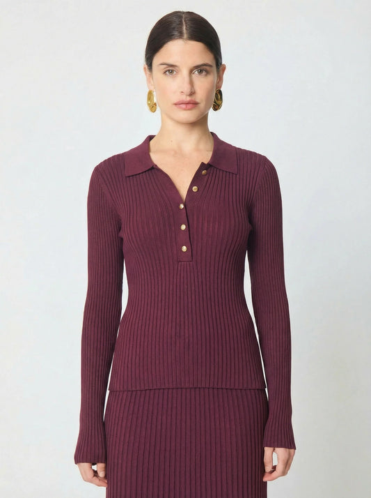 A woman modeling a ribbed long-sleeve polo shirt in deep burgundy with gold buttons, paired with a matching ribbed skirt, against a light gray studio background.