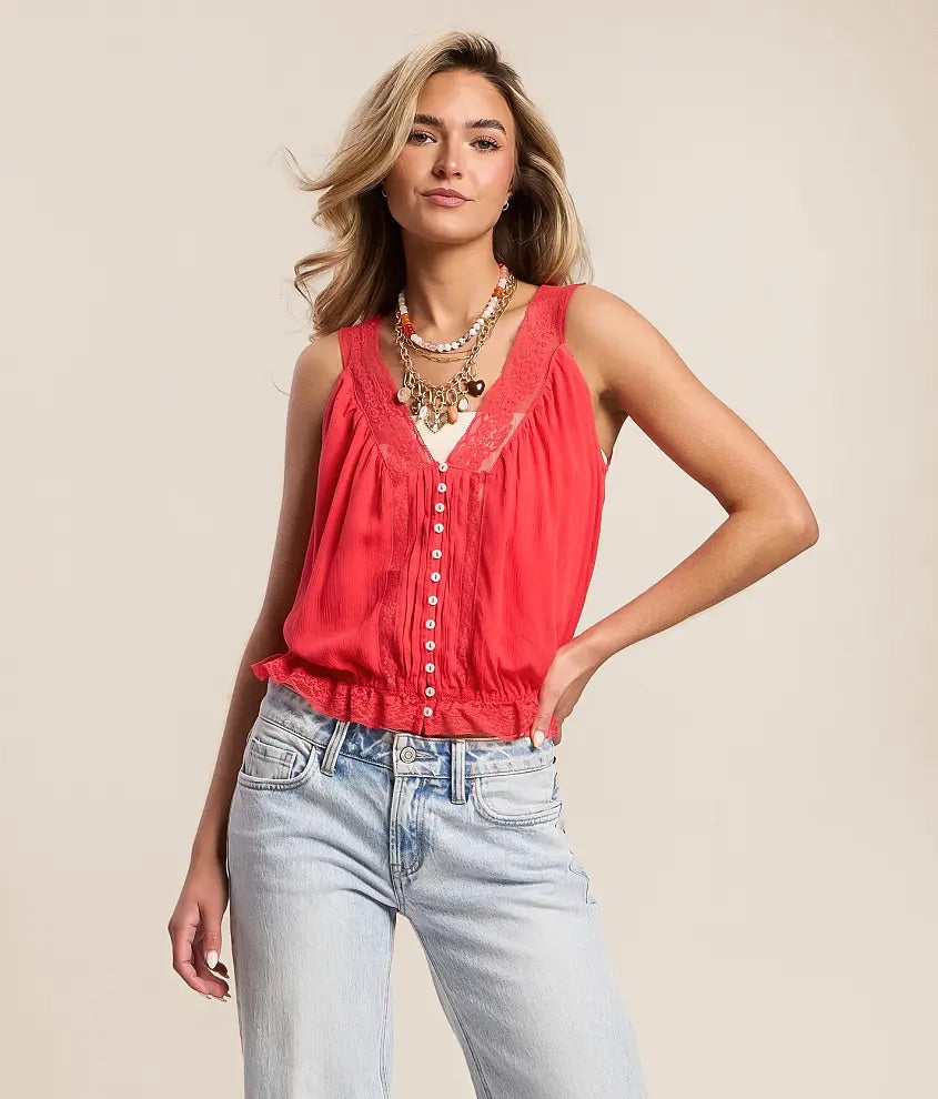 Woman wearing a red sleeveless top and blue jeans against a beige background