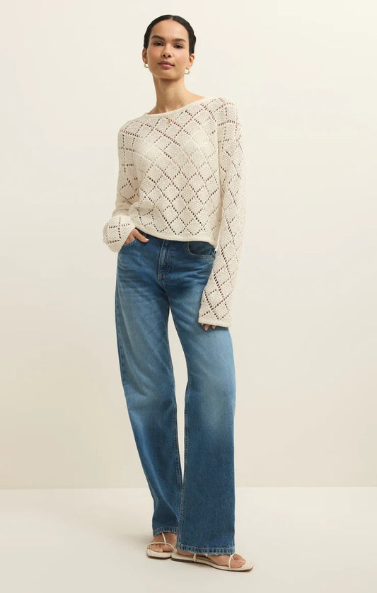 Woman wearing a beige knitted sweater and blue jeans on a plain background