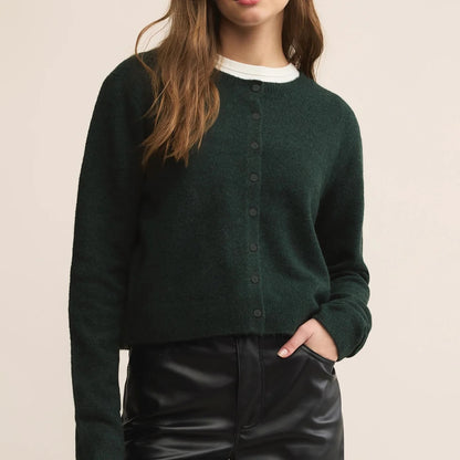 Person wearing a dark green cardigan over a white shirt with a beige background