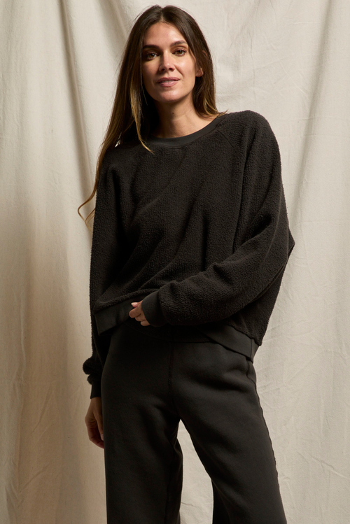 Woman wearing a black sweater and pants against a beige curtain background