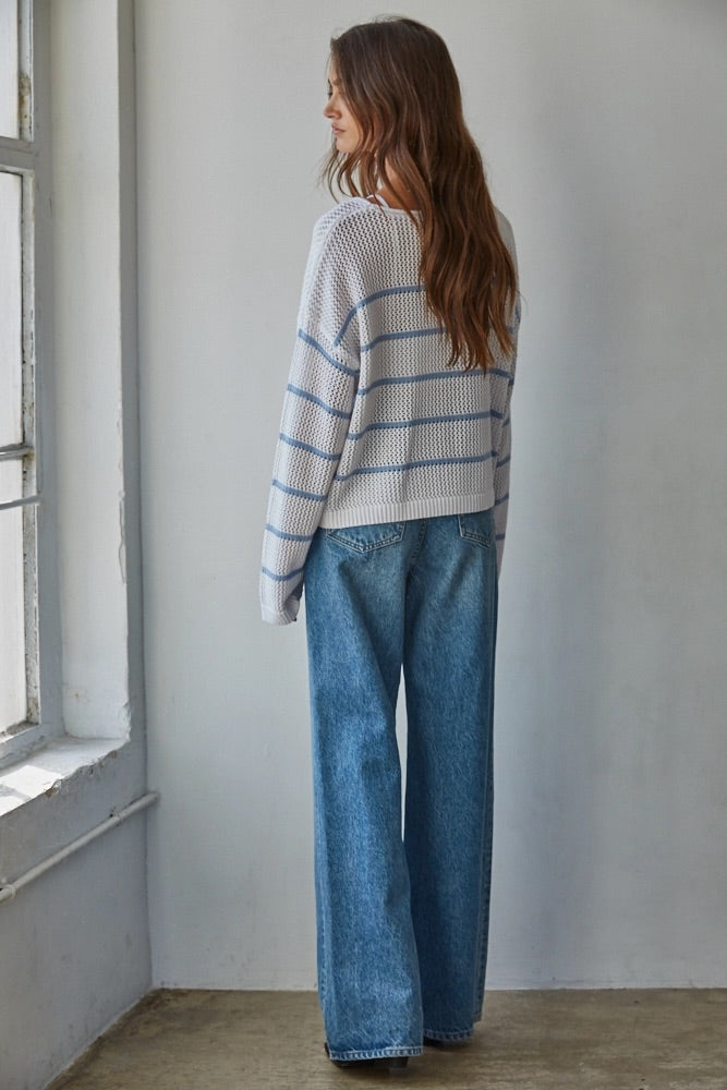 Woman wearing a striped sweater and blue jeans standing in a room with a window.