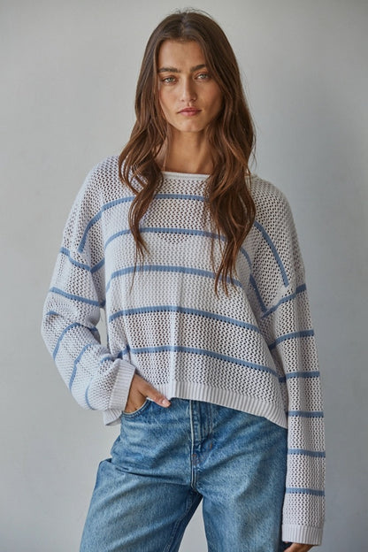Woman wearing a striped sweater and jeans against a gray background