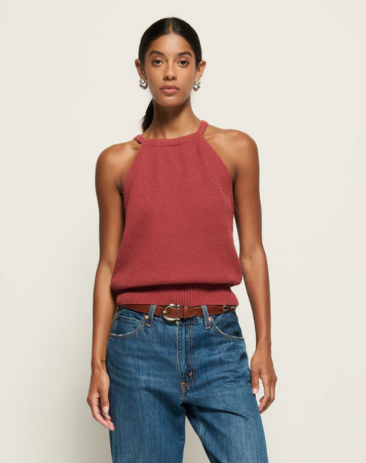 Woman wearing a red sleeveless top and blue jeans against a plain background