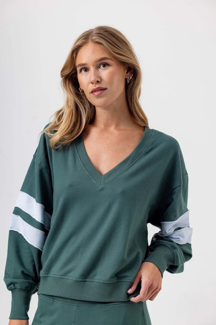 Woman wearing a green sweatshirt with white stripes on a plain background