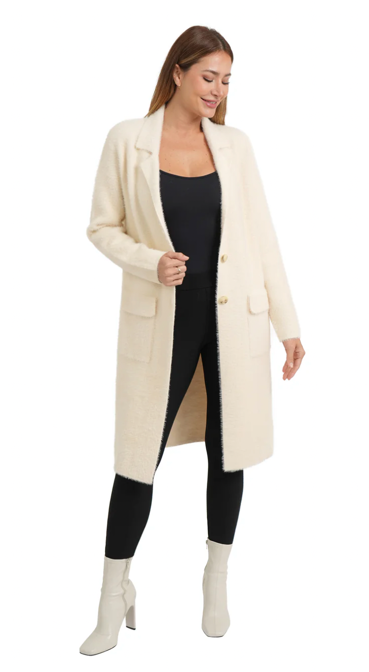 Woman wearing a long cream coat over a black outfit on a white background