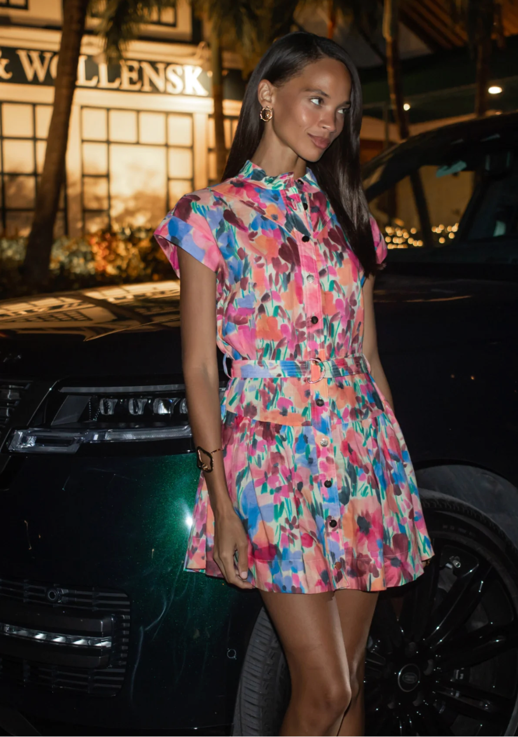 Woman in a colorful dress standing next to a car at night.